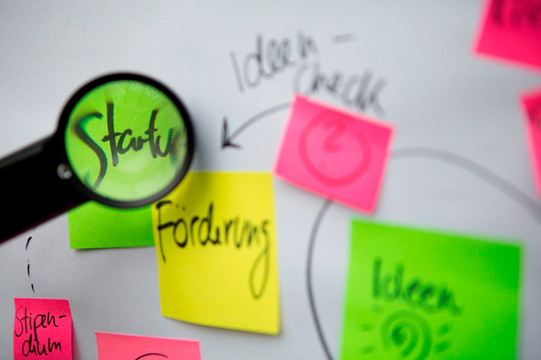 Beschriftete bunte Klebezettel und eine Lupe, die die Schrift vergrößert.