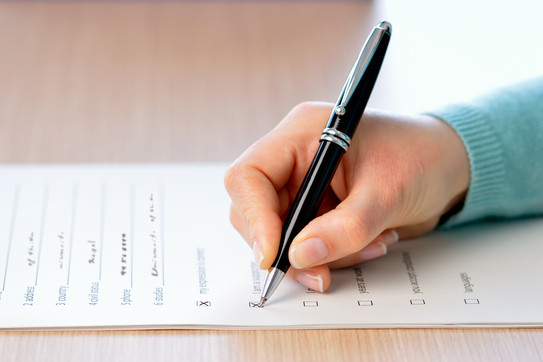 A hand holding a pen fills out a survey questionnaire.