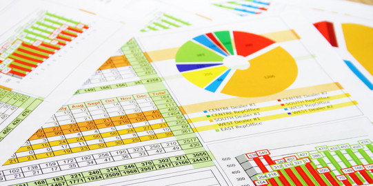 Paper pages with tables, pie charts, column charts as well as graph charts lie on top of each other.
